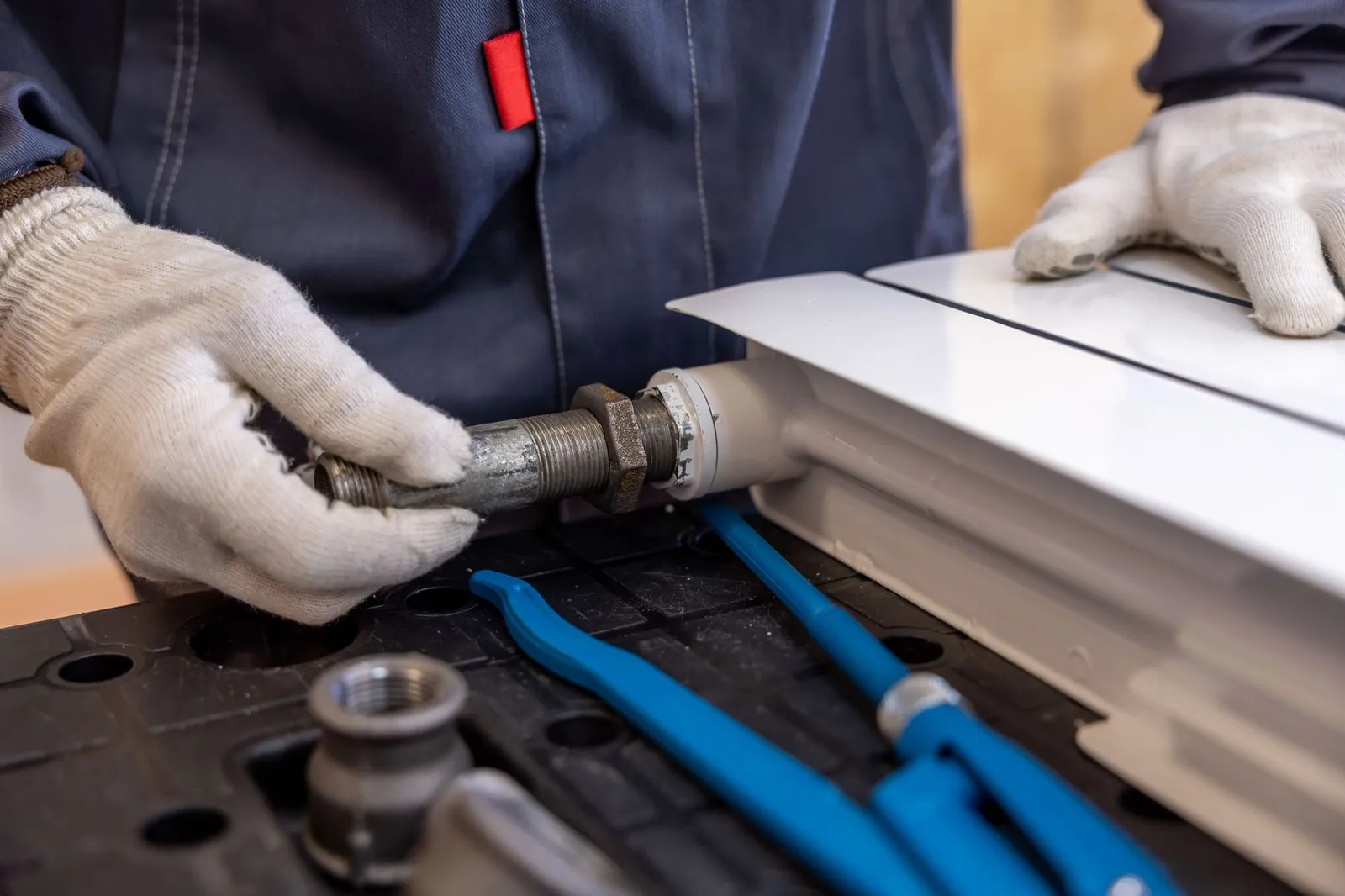 A plumber in work gloves fits a pipe connection