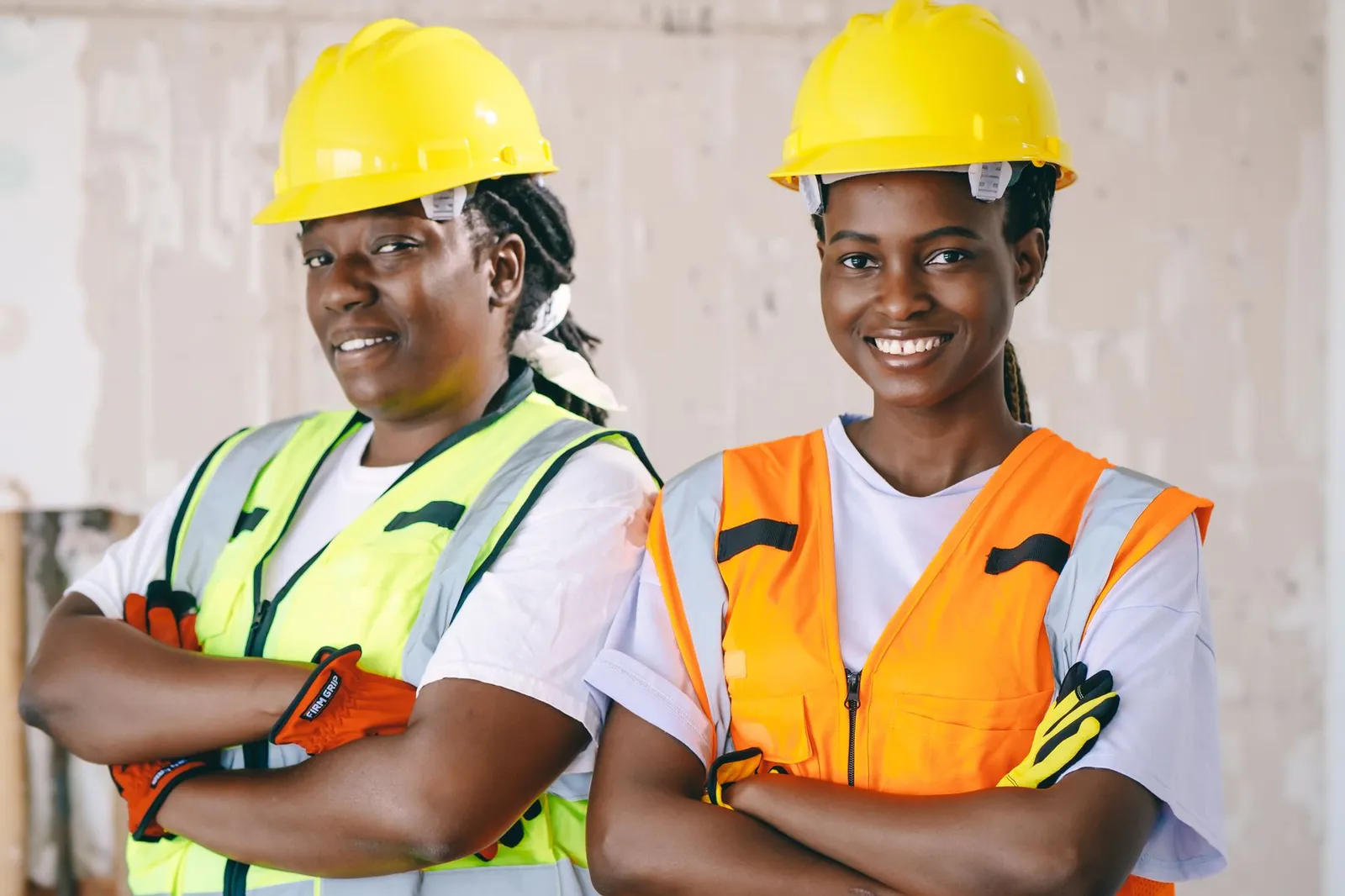 Two women in yellow hard hats and reflective vests on a job site
